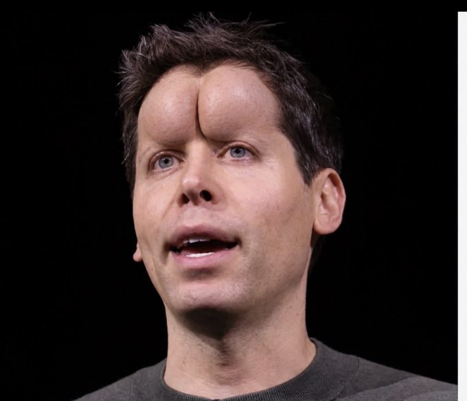 A portrait photo of a man with short dark hair against a black background, edited to show an unusual prosthetic or mutation on his forehead resembling a small second nose or horn-like growth above his eyebrow.