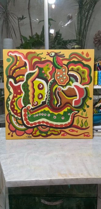 A colorful, abstract acrylic painting with green, orange, red, and yellow patterns displayed on a small easel in an art studio.