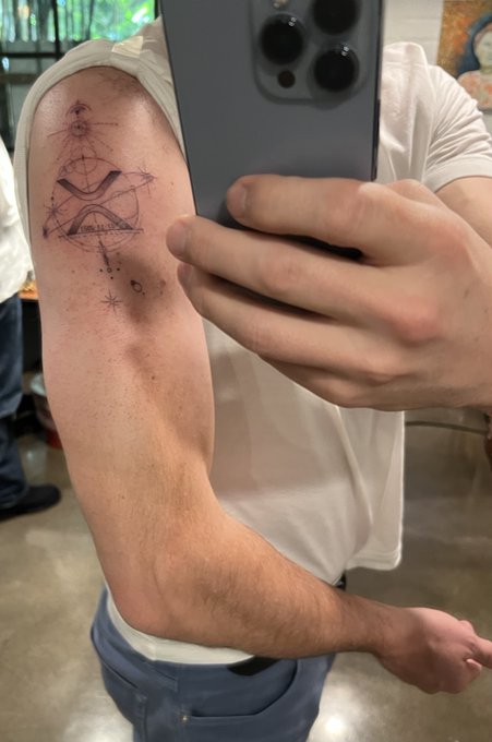 A person takes a mirror selfie showing a freshly inked tattoo on their upper arm featuring cosmic/celestial designs including geometric shapes, stars, and what appears to be planetary alignments, perfectly complementing the post about the rare planetary alignment and solar eclipse symbolizing a cosmic reset for XRP.