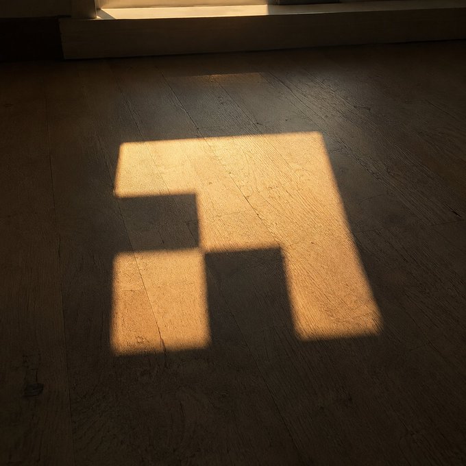 A square patch of warm sunlight cast onto a wooden floor, creating a bright geometric shape against the darker surrounding planks.