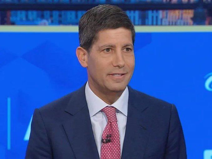 A news anchor in a navy suit and pink patterned tie appears on a broadcast set with blue background graphics, likely reporting on the just-released US CPI data showing inflation came in line with expectations at 3.4%.