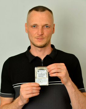 The image features a man holding an old floppy disk, possibly a hard drive or a USB drive, with his hands. The man appears to be wearing a black shirt and has a bald head. The photo also includes text that reads "Bitcoin hard drive worth $950M lost forever", which is likely related to the Bitcoin cryptocurrency. This information suggests that the image might have been taken during an event or discussion about Bitcoin or digital currency, possibly as part of a presentation or exhibition.

The man holding the floppy disk and the Bitcoin-related text create a connection between the physical object (the floppy disk) and the digital world (Bitcoin). The juxtaposition of these two elements highlights the contrast between the tangible and the virtual aspects of our lives in the modern era.