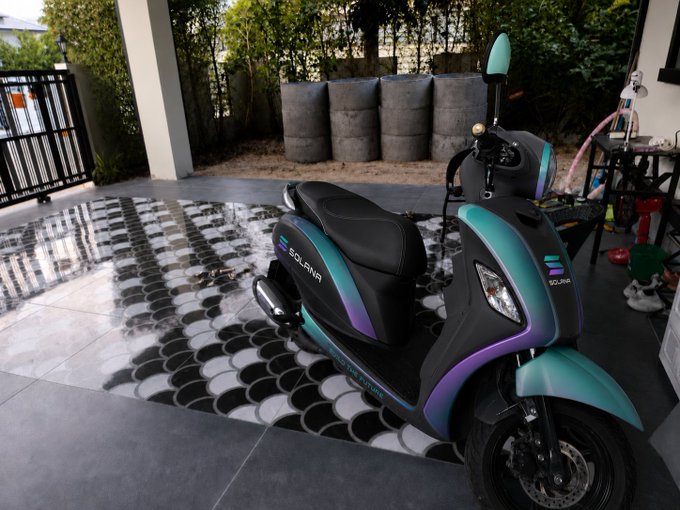 A black and teal Solina scooter with purple accents parked on a patterned outdoor mat in a courtyard setting with concrete planters.