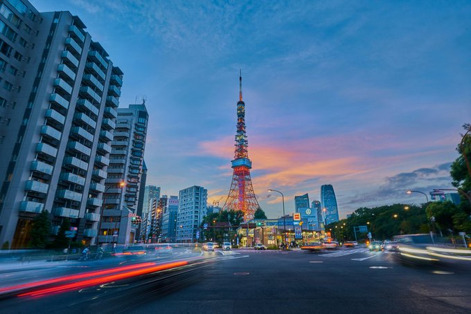 The image shows Tokyo Tower illuminated against a twilight sky, with streaks of light from passing traffic on a busy street below. The scene visually anchors the post's discussion of Japan's evolving regulatory landscape for digital assets, as the iconic landmark represents the very market where the new 20% flat tax and clearer Bitcoin ETF framework are taking shape.