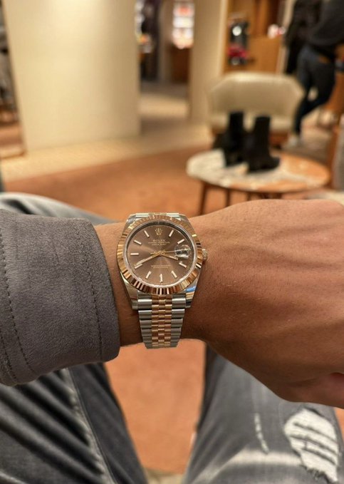 A close-up of a two-tone Rolex Datejust watch with a chocolate dial and fluted bezel worn on a person's wrist.