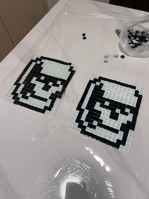 Two pixel art mosaics depicting characters made from small black and white square tiles laid out on a plastic-covered surface.