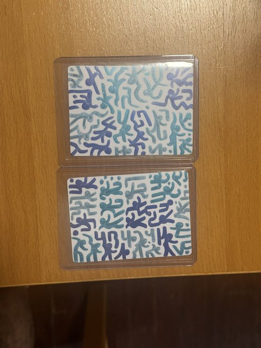 Two sealed trading cards featuring blue and purple abstract line art designs placed on a wooden surface.
