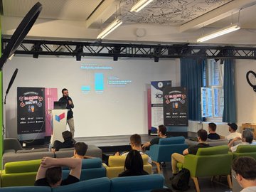 A presenter stands on stage delivering a keynote at "Telekom & Friends Vol.3" in Berlin, with a projection showing a chart titled "Growth of DAI Holders" and XDC network banners visible. The image captures the institutional Web3 event where XDC gave the opening keynote on real-world asset infrastructure, as attendees watch from colorful seating in a modern conference room.