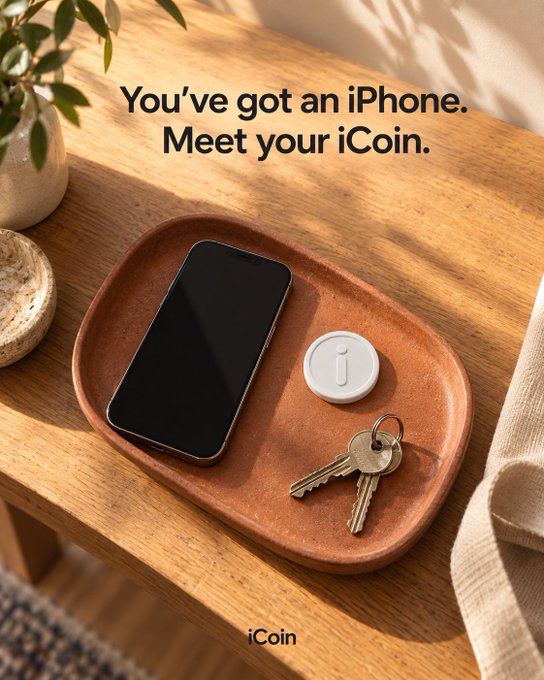 An advertisement displays the text 'You've got an iPhone. Meet your iCoin.' above a terracotta tray holding an iPhone, a small round white device labeled 'iCoin', and keys on a wooden table.