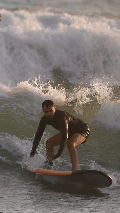 A man in a wetsuit balances on a surfboard while riding a crashing wave, surrounded by ocean spray.