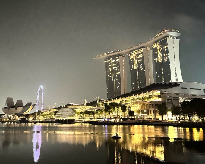A nighttime cityscape of Singapore's Marina Bay featuring the illuminated Marina Bay Sands hotel towers, the ArtScience Museum, and the Singapore Flyer Ferris wheel.