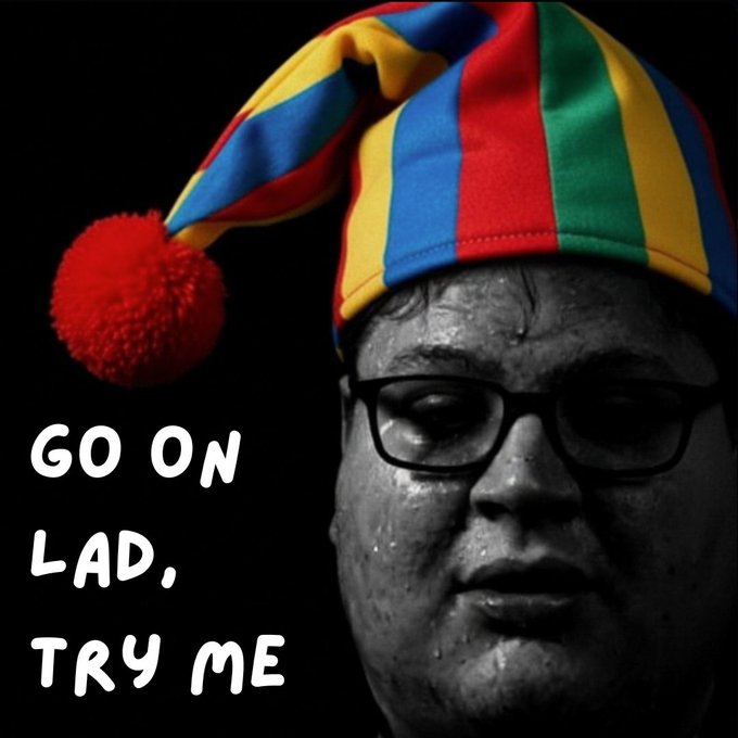A black-and-white portrait of a man wearing glasses and a colorful jester hat with a red pom-pom, with the text 'GO ON LAD, TRY ME'.
