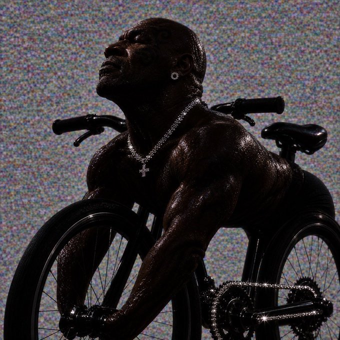 A muscular, glistening dark-skinned man with face tattoos, diamond earrings, and a cross necklace is posed suggestively straddling a black bicycle against a glitchy static background. The image ties to the post's reference to $biketyson, a meme-inspired crypto token, with the shirtless figure and bike serving as a literal depiction of the token's namesake.