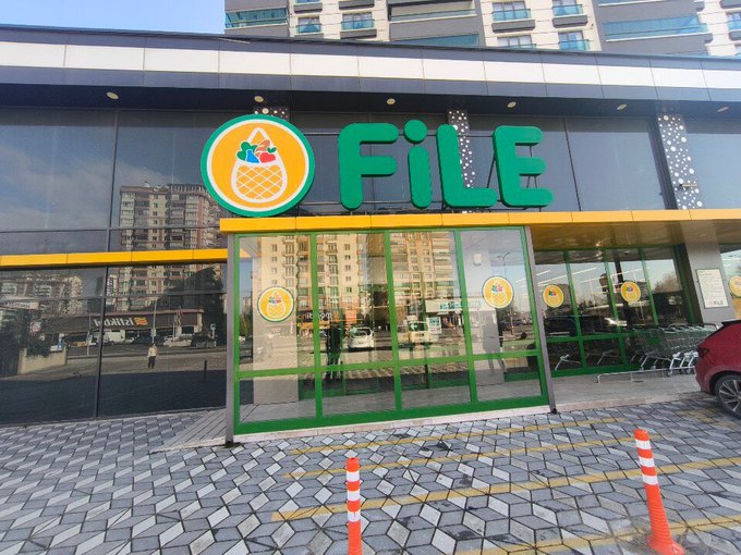 The image shows the storefront of a FiLE supermarket, with its bright green signage and pineapple logo, featuring glass doors and shopping carts visible at the entrance. This appears to be the grocery store where the poster went shopping for their marriage market haul using a reusable bag.