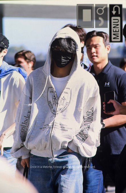 An interface overlay showing a photo of a person wearing a grey hoodie, face mask, and sunglasses surrounded by a crowd, with a menu icon in the top right and footer text reading "Once in a lifetime, forever proof. All rights reserved."