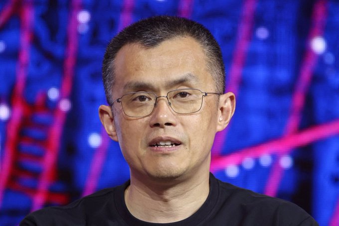 A close-up portrait of a man wearing glasses and a black shirt, photographed against a blue-toned illuminated background.