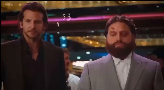 The image features two men dressed in suits standing next to each other. One of them has a beard and appears to be balding. They are both wearing ties, indicating that they might be attending a formal event or a business meeting. The background shows a neon sign with numbers on it, which could possibly represent some sort of data or information relevant to the image's context.