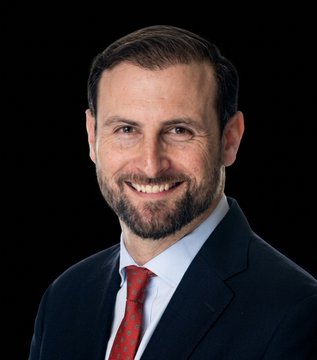 The image features a man wearing a suit, tie, and red shirt with a beard. He has a smile on his face as he looks directly at the camera. The background of the photo is black, which contrasts with the white text that reads "July 4th". This suggests that July 4th is the target date for passing the Clarity Act, as indicated by the post's title.