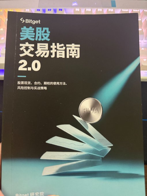 A photograph of a booklet titled 'Bitget 美股交易指南 2.0' (US Stock Trading Guide 2.0) resting on a backlit keyboard, featuring an RWA coin graphic.