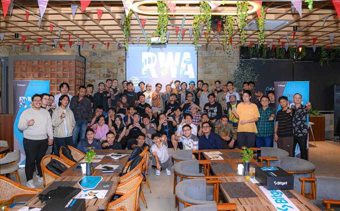 A large group of people poses for a group photo at an event with 'RWA' and 'polygon' branding visible on screens and banners.