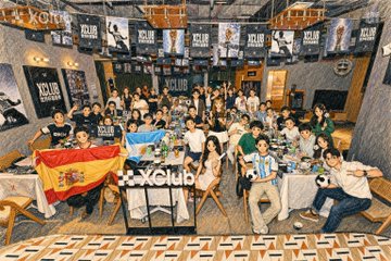 A large group photo of a club gathering, with attendees posing around tables beneath banners that appear to read 'JCLUB'.