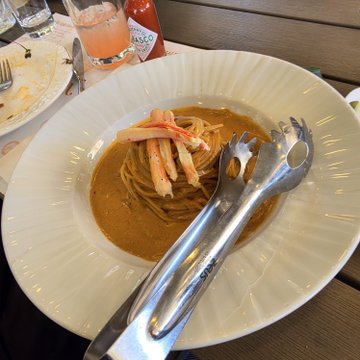 A bowl of crab pasta in a creamy orange sauce served with tongs in a white fluted bowl.