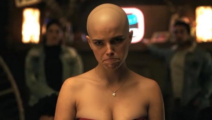 The image shows a bald woman with a necklace, standing in front of a neon sign that reads "sol". She has a serious expression on her face as she looks directly at the camera. The caption for this image includes the words "bro didn't wanna include sol" and "focus on what is in the image".