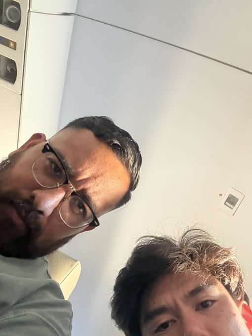A man wearing glasses takes a selfie alongside his freshly groomed son, showing off the boy's clean haircut after their barber visit that turned into an unexpected crypto consultation. The barber, inspired by their Twitter posts about memecoins, asked for trading recommendations mid-haircut.