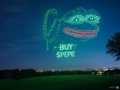 A nighttime photo of a grassy field where a glowing projection of a cartoon monster face with the text "-BUT- Boo!" is displayed against the dark sky.