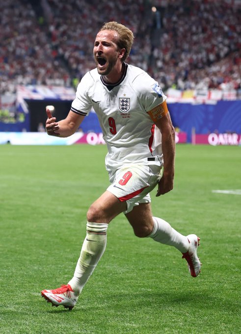 Harry Kane, wearing England's #9 jersey with a captain's armband, celebrates passionately with a thumbs-up on the pitch, embodying the post's message of perseverance and late-game triumph.