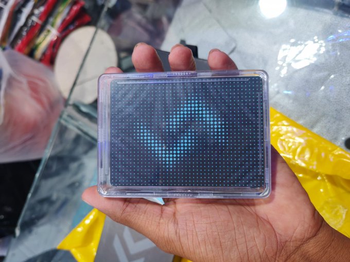 A hand holding a clear plastic case containing a blue LED pixel display screen.