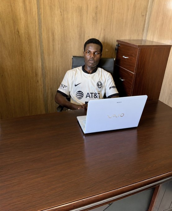 A young man wearing an America soccer jersey with 'AT&T' sponsor logo sits at a desk using a white VAIO laptop.
