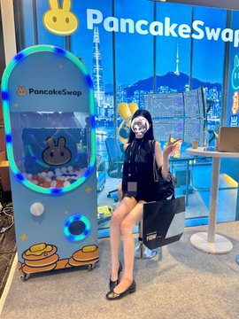 A woman in a black dress and bunny ears poses next to a "PancakeSwap" branded claw machine at an event for @kbwofficial, connecting the crypto project's digital community presence to an in-person gathering as "proof of community."