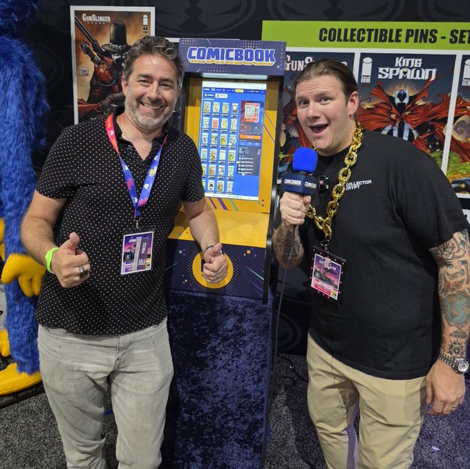 Two men smile and pose at a ComicBook Collectibles booth featuring Gunslinger Spawn and King Spawn merchandise, with one man holding a ComicBook microphone.