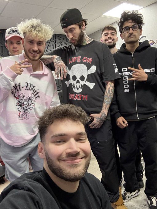 The image shows a group selfie of six young men posing together, with one in a pink "Off-White" sweater and another prominently wearing a black "LIFE OR DEATH" skull t-shirt. The casual group photo pairs with the post's playful suggestion that this crew should be recruited by Robinhood to tackle crypto scams and boost the market.