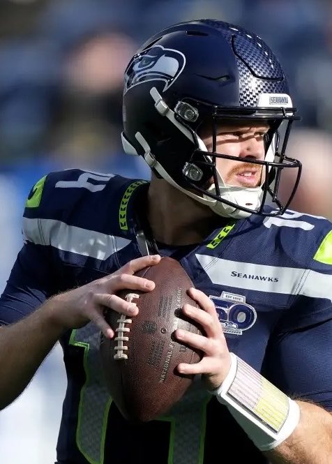 A Seattle Seahawks quarterback, wearing a navy helmet with the Seahawks logo and a jersey marked with the number "10" and "SEAHAWKS" text, prepares to throw an NFL football. The image relates to the post by showcasing the #1 team in Tom Brady's power rankings, as the Seahawks top his list following Week 1 of the NFL season.