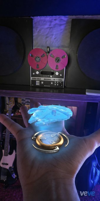 The image features a hand holding up a coin that has the words "VeVE" written on it. The coin is made of metal, with a unique design featuring a blue flower at its center. The background shows an old-fashioned stereo system, which adds a vintage touch to the scene. The post discusses scarcity and relevance in relation to Bitcoin, specifically mentioning the limited number of Falcon Millennium Holodisks available for purchase as an example.