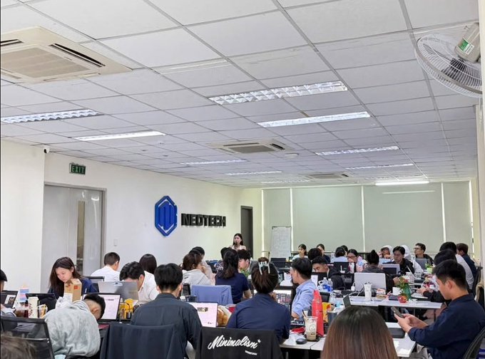 A crowded office scene shows numerous employees working on laptops, with a "NEOTECH" logo displayed on the wall and a person wearing a "Minimalism" jacket visible in the foreground. The image illustrates the Neotech trading platform that the post warns against, cautioning followers about copy trade and VIP signal scams that have caused many investors to lose their funds.