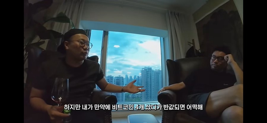 Two men sit in a high-rise apartment discussing Bitcoin investments, with one gesturing while holding a wine glass, as the Korean subtitle reads "하지만 내가 만약에 비트코인 4개 샀다가 반값되면 어떡해" (But what if I bought 4 bitcoins and it gets cut in half). The image captures a moment of financial anxiety about Bitcoin volatility, which aligns with the post's distressed tone about lacking even 0.1 Bitcoin or 10 million won to buy.