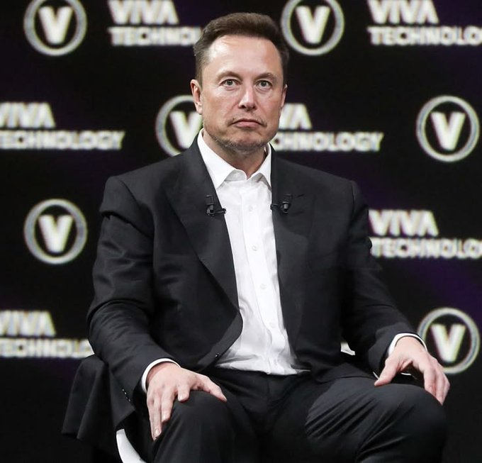 The image shows a man wearing a suit sitting down, possibly at a public event or press conference. The man's attire consists of a black suit with white collared shirt underneath. There are logos visible in the background, including "SpaceX", which implies that the man might be involved in the company related to space exploration or technology. Additionally, there is a text that reads "Space X’s IPO valuation will equal the size of the entire Bitcoin and crypto market excluding stablecoins". This suggests that the man may be addressing a topic directly related to this specific event or conference. The image does not provide enough context to determine if he's actually speaking at such an event, but it is possible given the presence of these elements in the background.