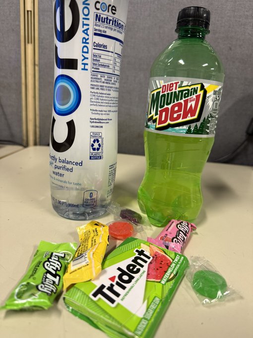 A bottle of 'Core Hydration' water and a bottle of 'Diet Mountain Dew' sit behind an assortment of candies including 'Laffy Taffy', 'Trident', and 'Sour Punch' on a table.