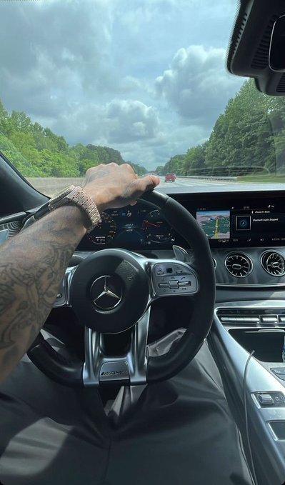 The image shows a person's arm inside a car, holding the steering wheel with both hands while driving down the road. There are no visible texts or other objects in the scene. The caption "Gmgm fam Happy Tuesday" appears to be unrelated to the main subject of the photo and is not directly related to the content being displayed on the screen.