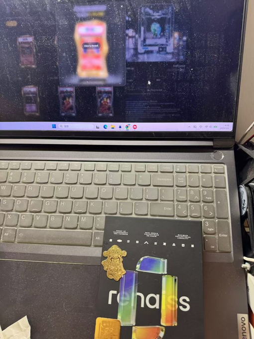 A Lenovo laptop is open on a desk displaying a screen, with a black package featuring holographic lettering spelling "romoss" and a gold lion-shaped seal resting on the keyboard.