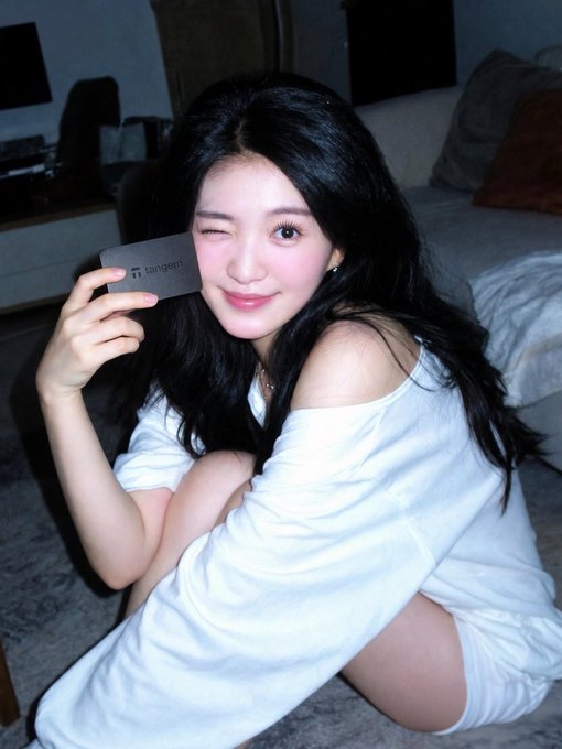A young woman with long dark hair winks and smiles while holding a card with 'tangem' printed on it near her face.