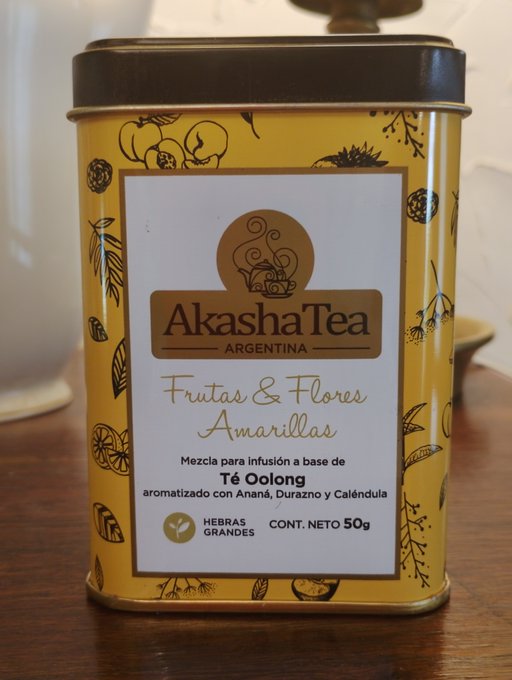 A yellow tin of Akasha Tea Argentina 'Frutas & Flores Amarillas,' an Oolong tea infusion blend with pineapple, peach, and calendula, net weight 50g, featuring 'Hebras Grandes' (large leaves).