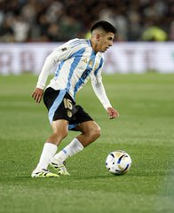 A soccer player wearing the Argentina national team jersey, featuring the number 16, controls the ball during a match. The white and light blue striped kit with the AFA crest represents the iconic Argentine football team.