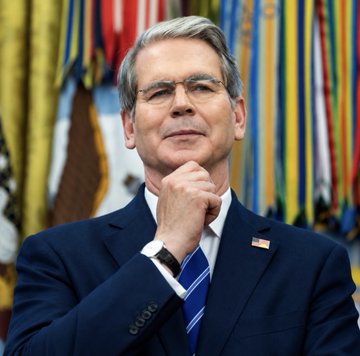 Scott Bessent, U.S. Treasury Secretary, stands before a backdrop of flags in a suit and tie. His official Treasury role connects to the post’s claim that the department bought back $750 million of U.S. debt, framed as bullish for Bitcoin ($BTC).