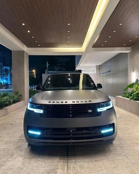 A silver Range Rover SUV with illuminated headlights is parked under a covered driveway entrance at night, with the 'RANGE ROVER' badge visible on the hood.