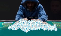A dealer at a casino table arranging multiple stacks of white and blue poker chips, with spectators in the background.