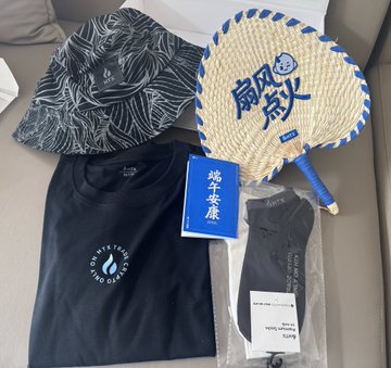 The image features a collection of items, including clothing such as t-shirts and hats, along with accessories like books and fans. The items are arranged on a table or couch, creating an assortment of objects that appear to be related to a theme or event. The presence of Asian characters in the image suggests that this could be a store display showcasing products from Asia or possibly a themed gathering where attendees can purchase these items as souvenirs or gifts.